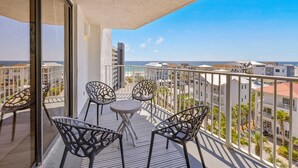 Un balcon avec une table et des chaises, donnant sur un paysage urbain avec des immeubles et des palmiers.
