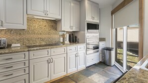 A modern kitchen with white cabinets, granite countertops, a built-in oven, and a trash can.
