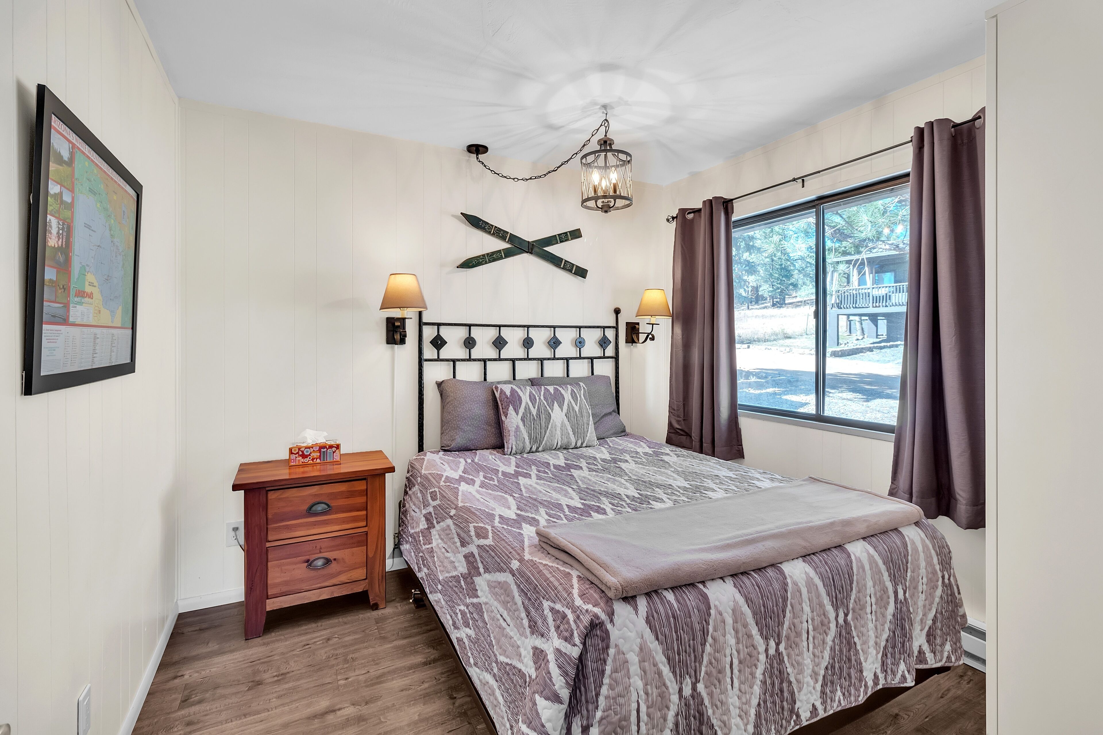 Un dormitorio con cama, dos lámparas de noche, una mesita de noche de madera, un mapa en la pared y una ventana con cortinas.
