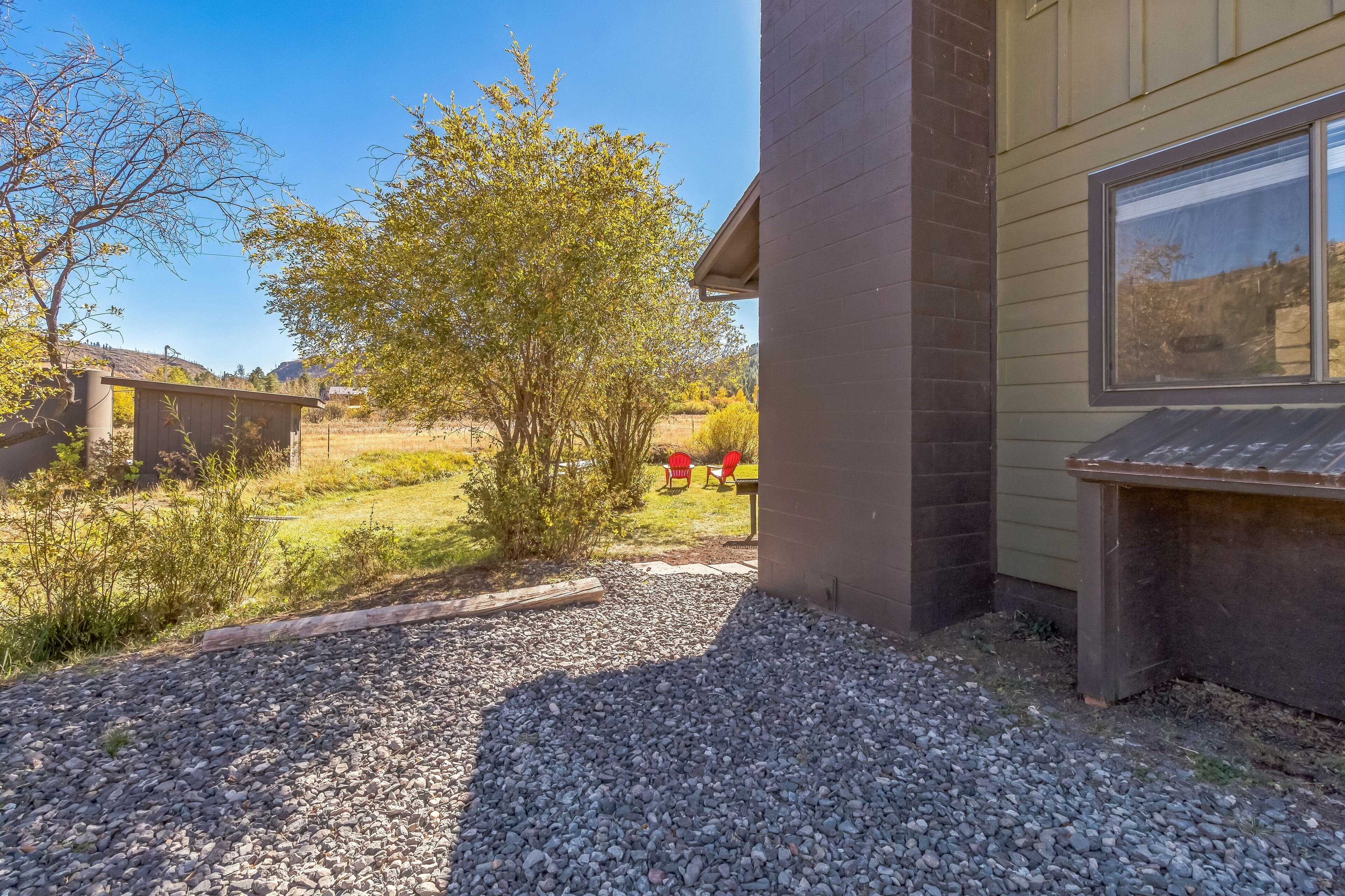 A building with a gravel driveway, a small tree, and a red chair in the background.
