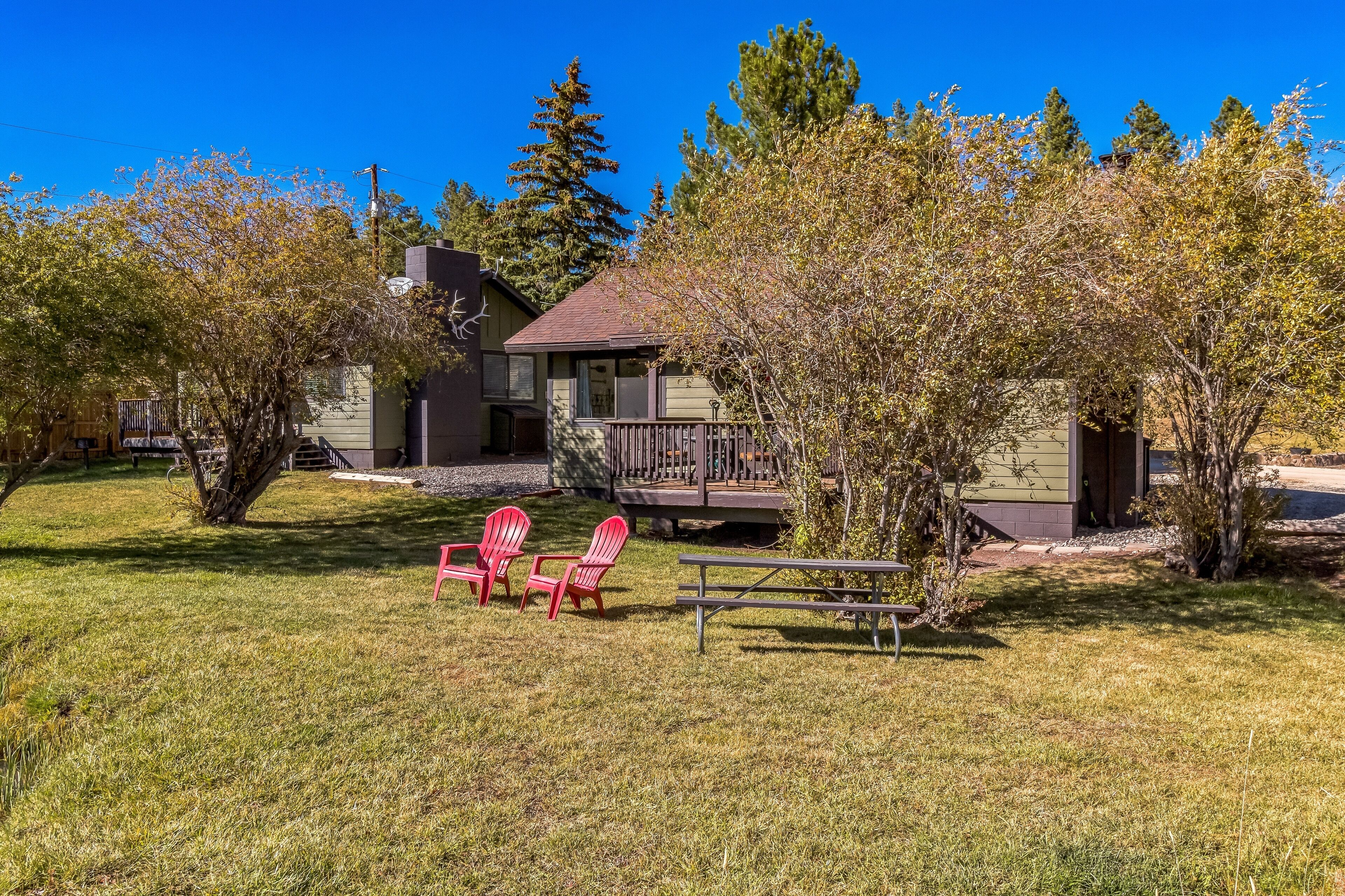 Ett hus med en veranda, två röda Adirondack-stolar och ett picknickbord på en gräsig trädgård.