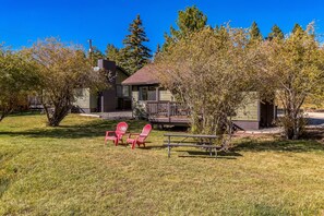 A house with a deck, two red Adirondack chairs, and a picnic table in a grassy yard.