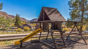 A playground with a slide and swings, surrounded by trees and a hilly landscape. - Cozy Cabin Retreat With Scenic Views 2 Bedroom Cabin (Greer)