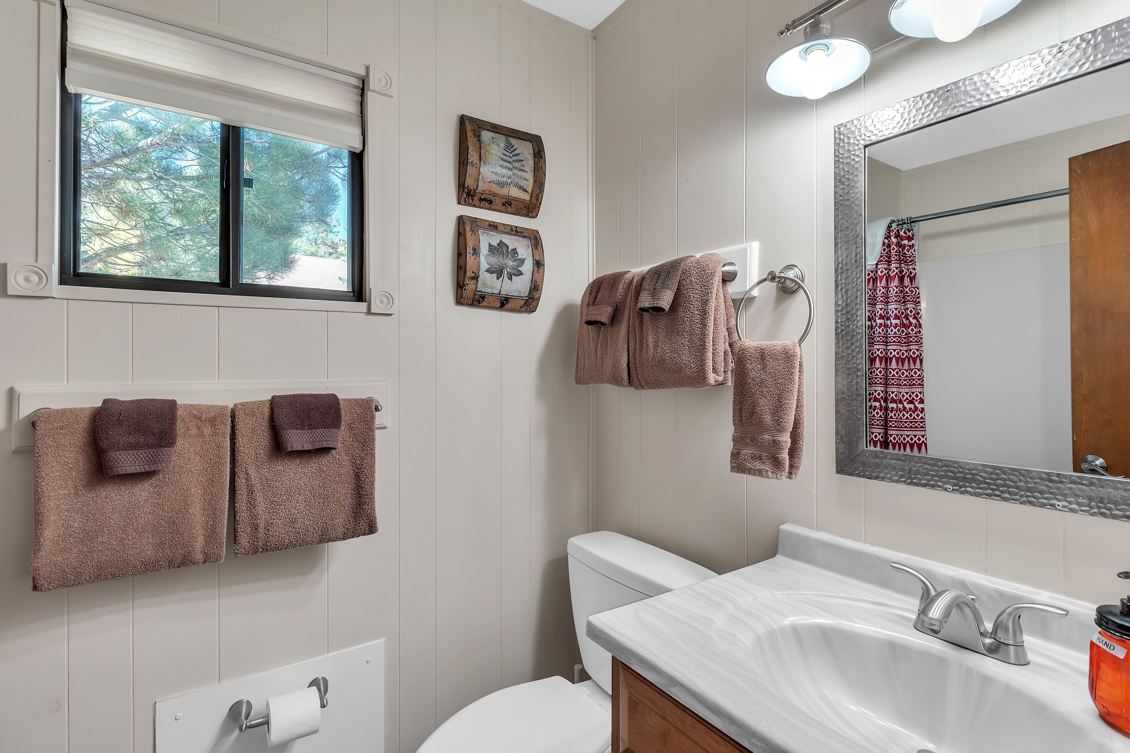 Une salle de bain avec un lavabo blanc, deux serviettes, des toilettes et une fenêtre avec des stores.