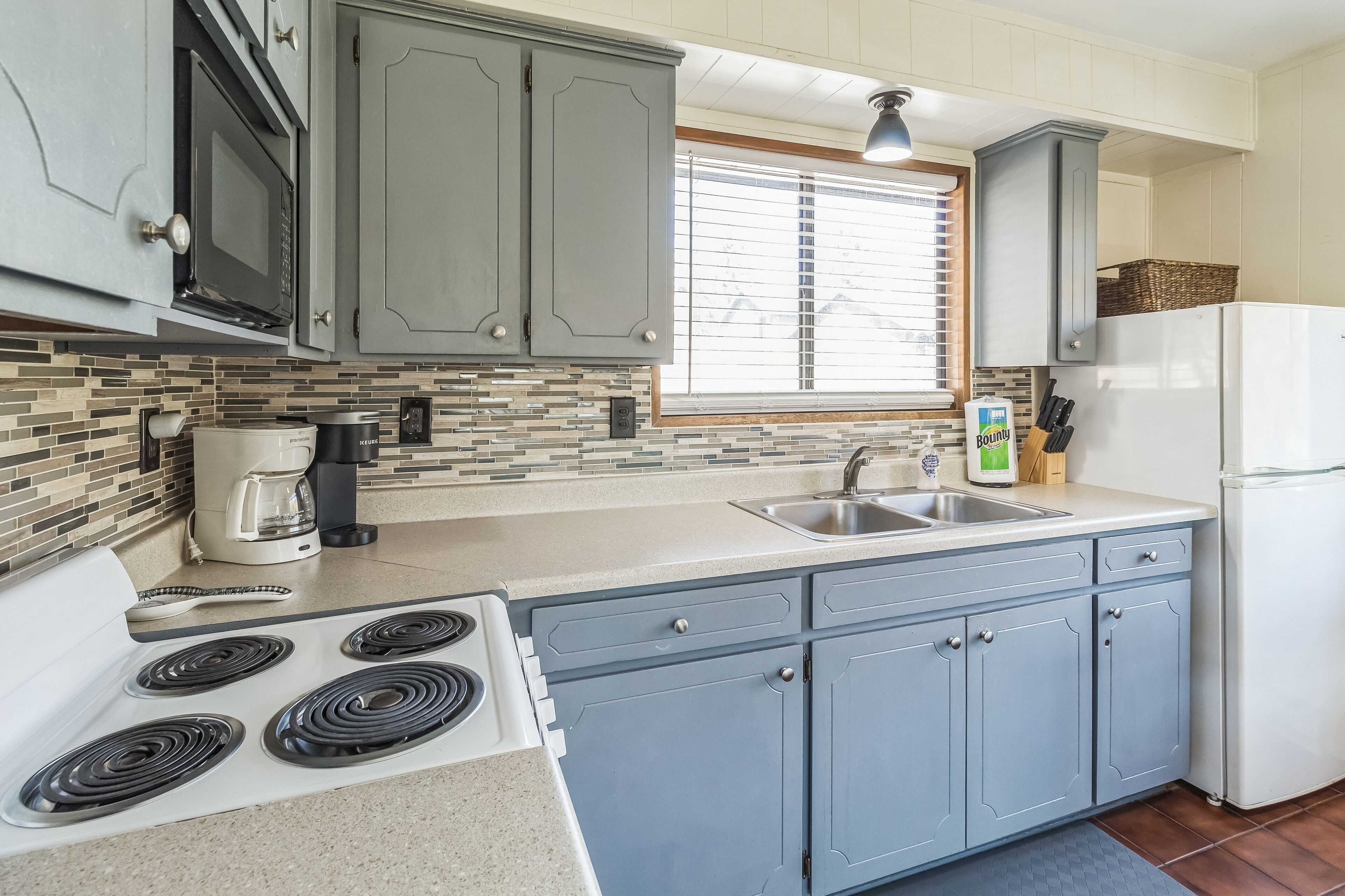 A kitchen with grey cabinets, a white stove, a coffee maker, and a refrigerator.