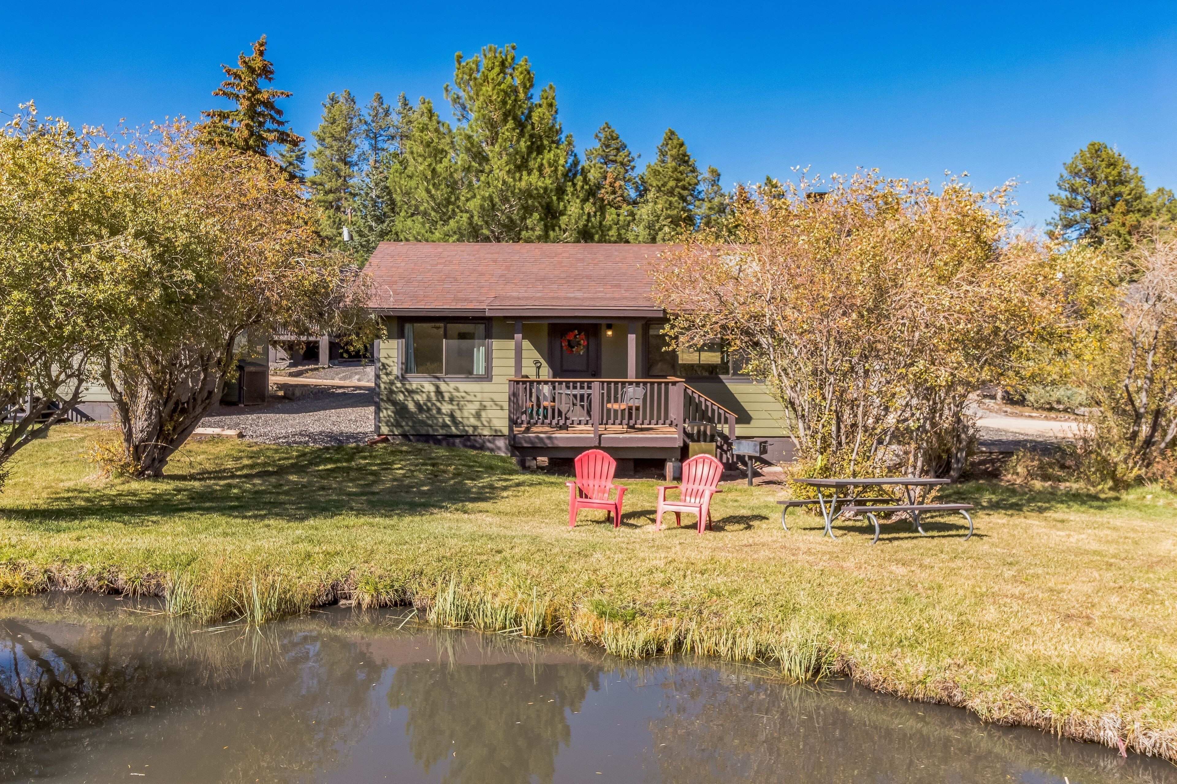Eine Lodge mit einer Terrasse, zwei roten Stühlen, einem Picknicktisch und einem Teich.
