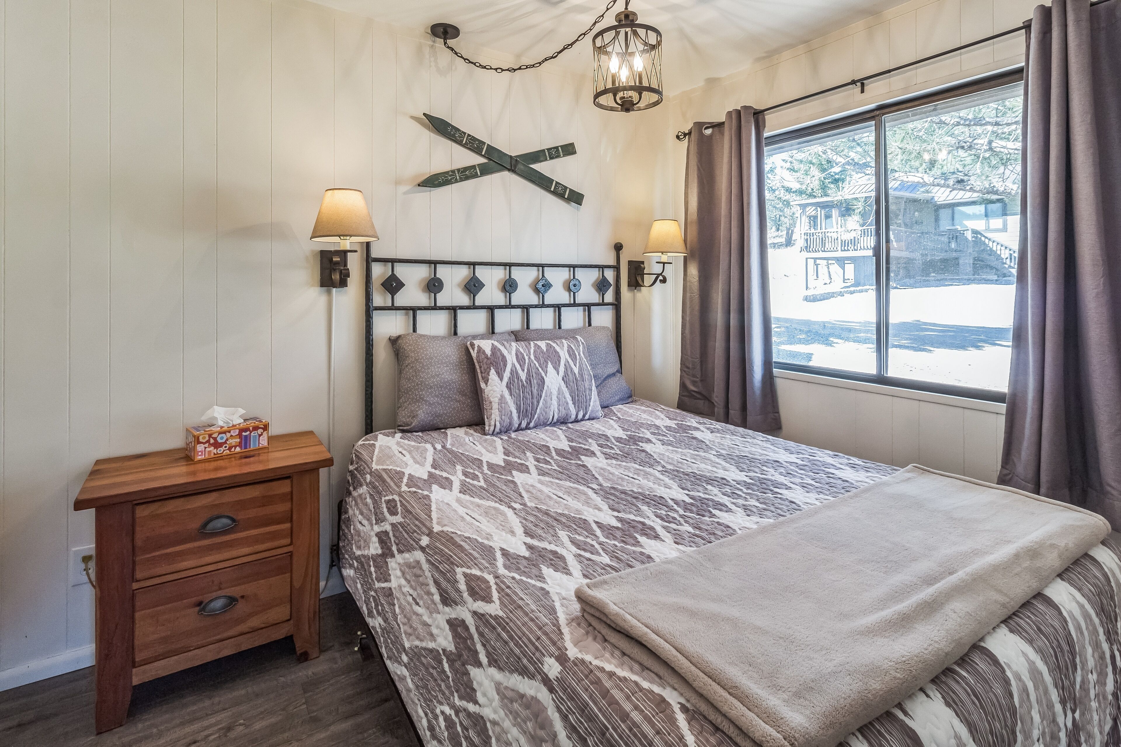 A bedroom with a bed, bedside lamps, a wooden nightstand, and a window with curtains.