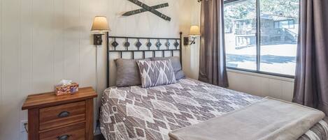 A bedroom with a bed, bedside lamps, a wooden nightstand, and a window with curtains.