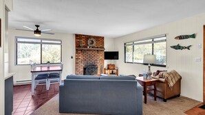 A living room with a brick fireplace, a sofa, a television, and a dining area with a table and chairs. - Cozy Cabin Retreat With Scenic Views 2 Bedroom Cabin (Greer)