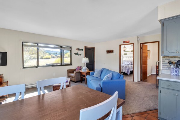 A cozy living room with a dining table, blue sofa, and a kitchen area with cabinets. - Cozy Cabin Retreat With Scenic Views 2 Bedroom Cabin (Greer)