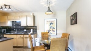 A modern kitchen with beige cabinets, a black tiled backsplash, and a glass dining table with four chairs. - E108 W Beaver Creek Blvd 2 Bedroom Condo (Avon)