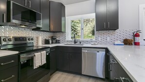 Una cocina moderna con armarios oscuros, electrodomésticos de acero inoxidable y una ventana con vistas a zonas verdes.