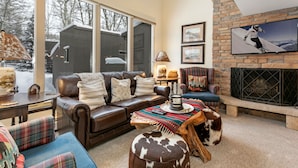 A cozy living room with a leather sofa, a plaid armchair, a wooden coffee table, and a fireplace. - Valley Condos A25 3 Bedroom Condo (Vail)