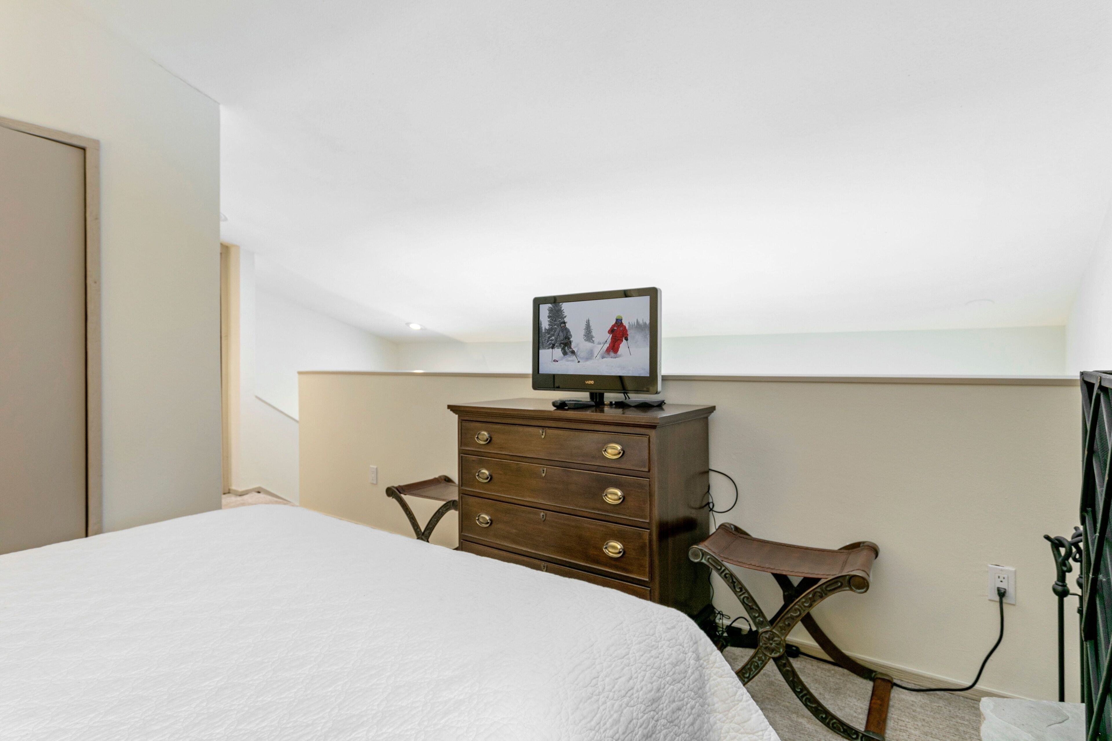 Ein Schlafzimmer mit einem Bett, einer Kommode, einem Fernseher darauf und einem Sessel.