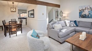 Ein Wohnzimmer mit grauem Ecksofa, einem Holztisch und einem Essbereich mit Holztisch und Stühlen.