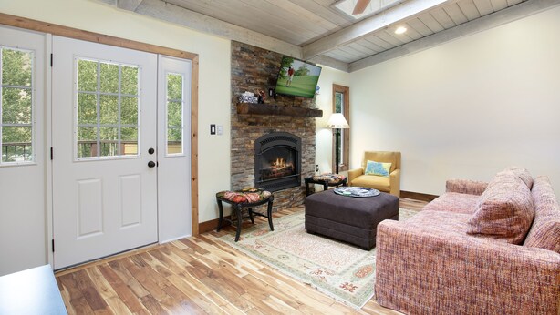 A cozy living room with a fireplace, wooden floors, and a ceiling fan.