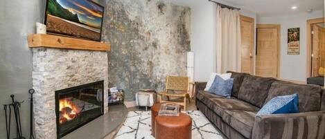 A living room with a stone fireplace, a sofa, a coffee table, and a television mounted above the fireplace.