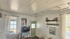 Quarto com sofá azul, televisão, mesa de jantar e janela com vista.