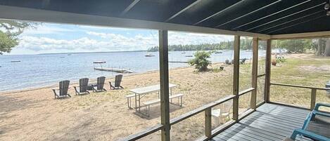 Une terrasse couverte offrant une vue sur une plage et un lac, avec des sièges d’extérieur et une table de pique-nique.