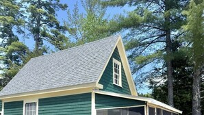A single-story house with a green exterior, a grey roof, and a covered porch area. - Friendly Inn Limit 5 3 Bedroom Cottage (Sebago)