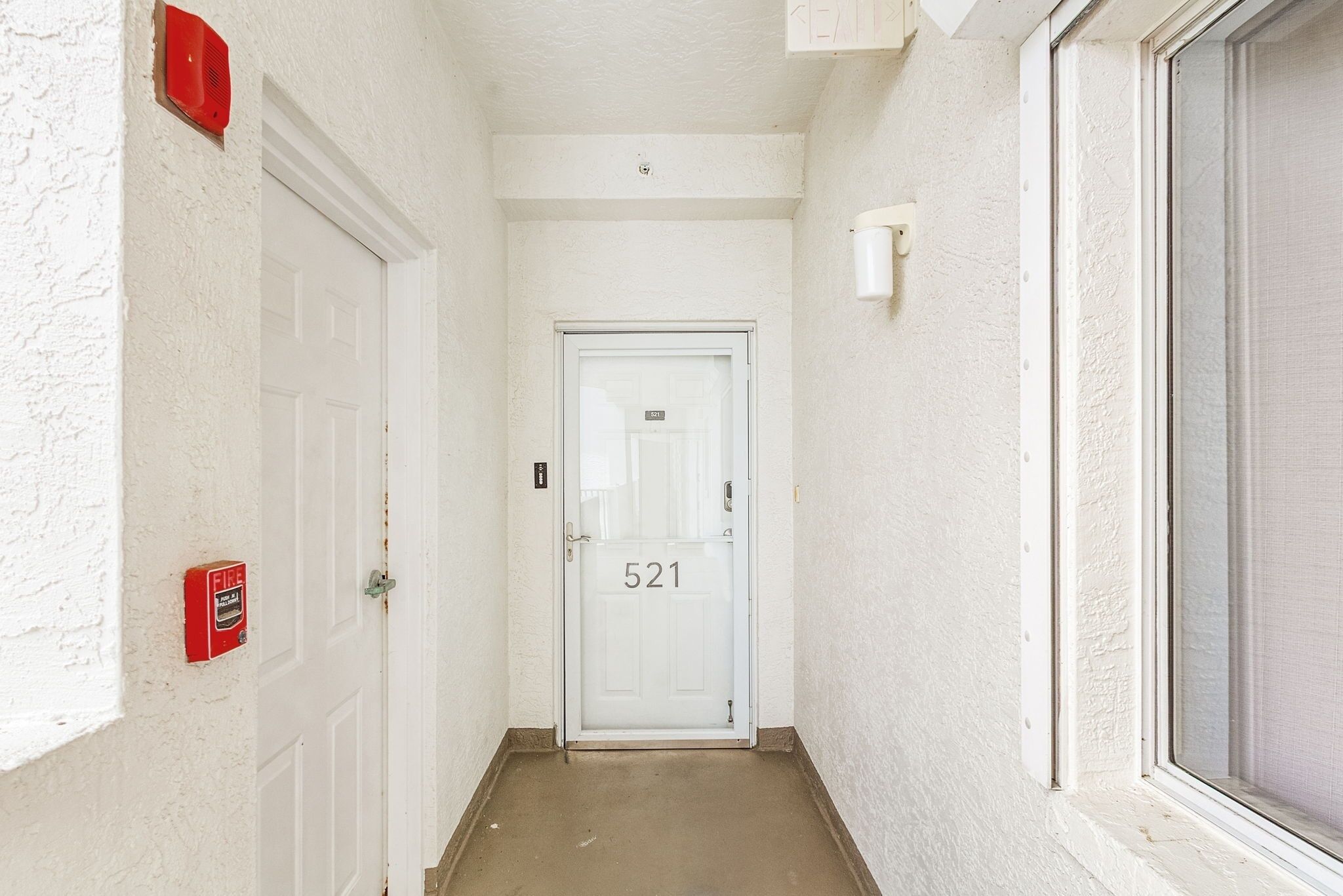 Un couloir étroit aux murs blancs, avec une porte blanche portant le numéro 521.