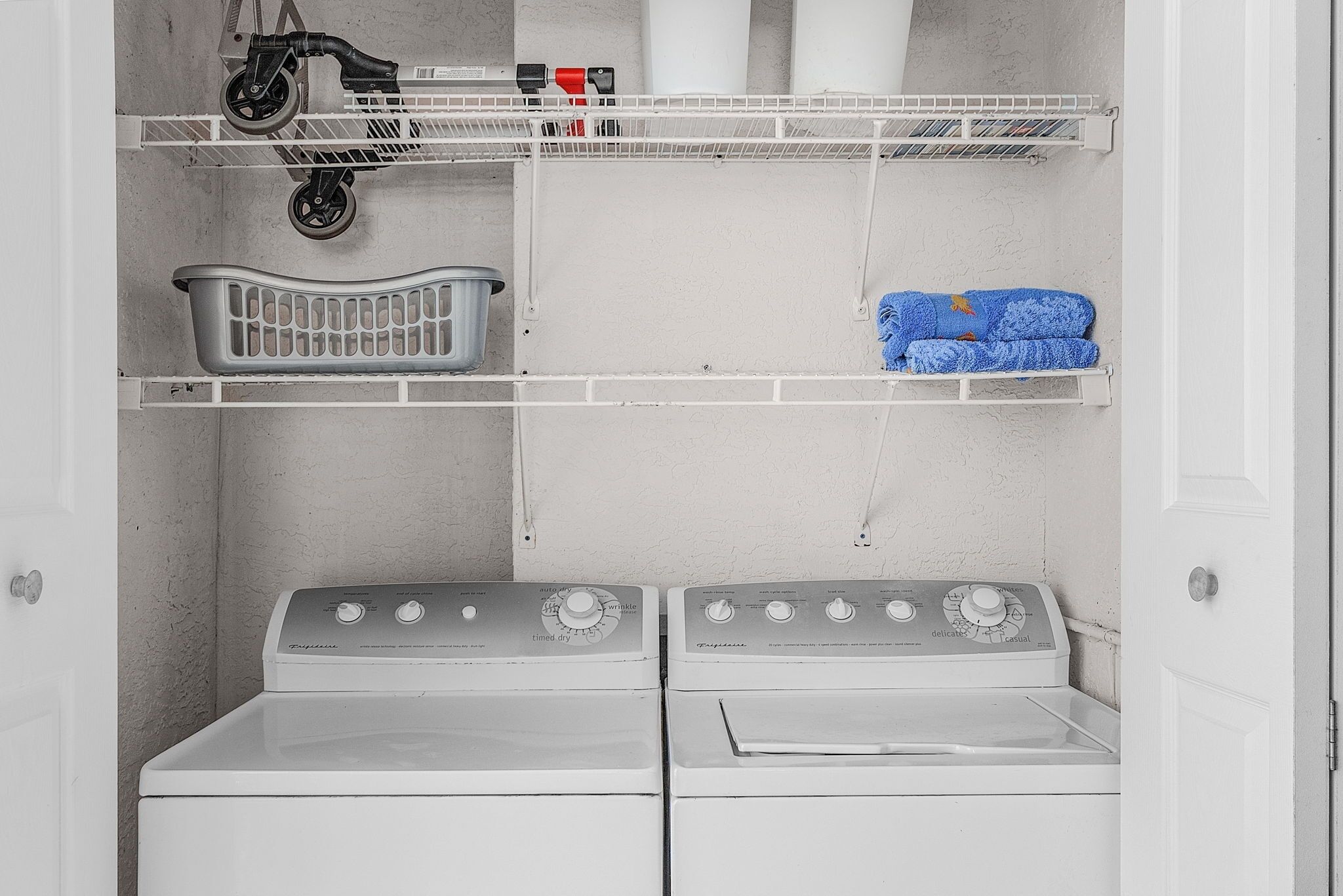 A laundry room with two stacked washers and dryers, a drying rack, and shelves with laundry supplies.