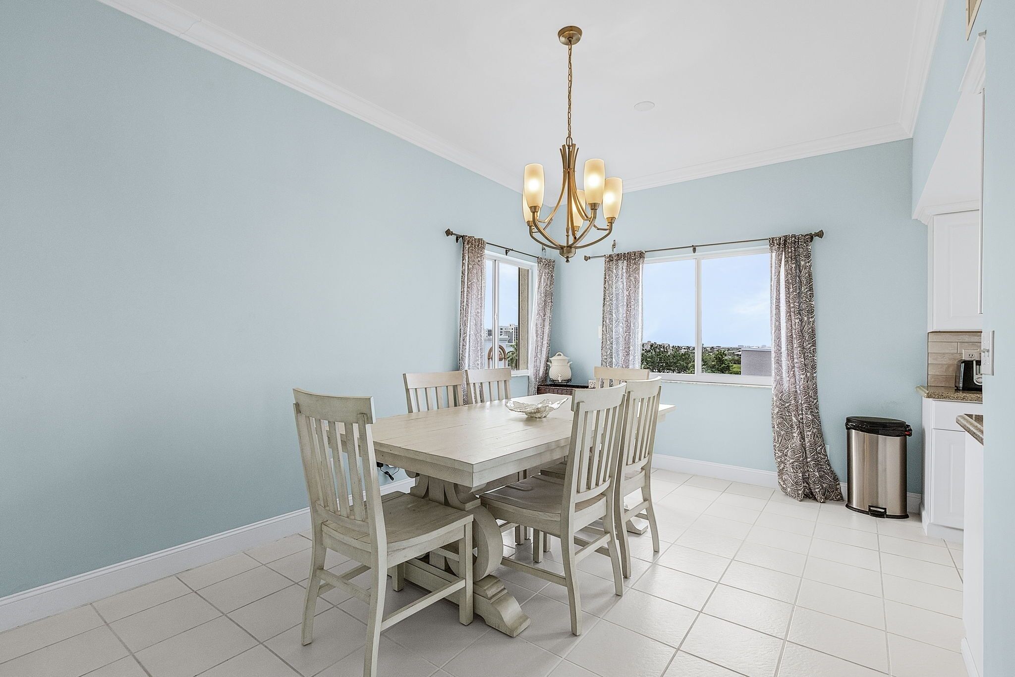 Un coin repas avec un mur bleu clair, un lustre, une table à manger avec des chaises et une fenêtre avec des rideaux.