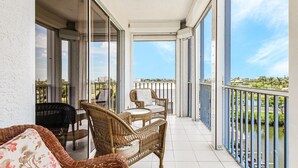 Ein Balkon mit Korbmöbeln, Glastüren und Blick auf einen Fluss und Grünflächen.