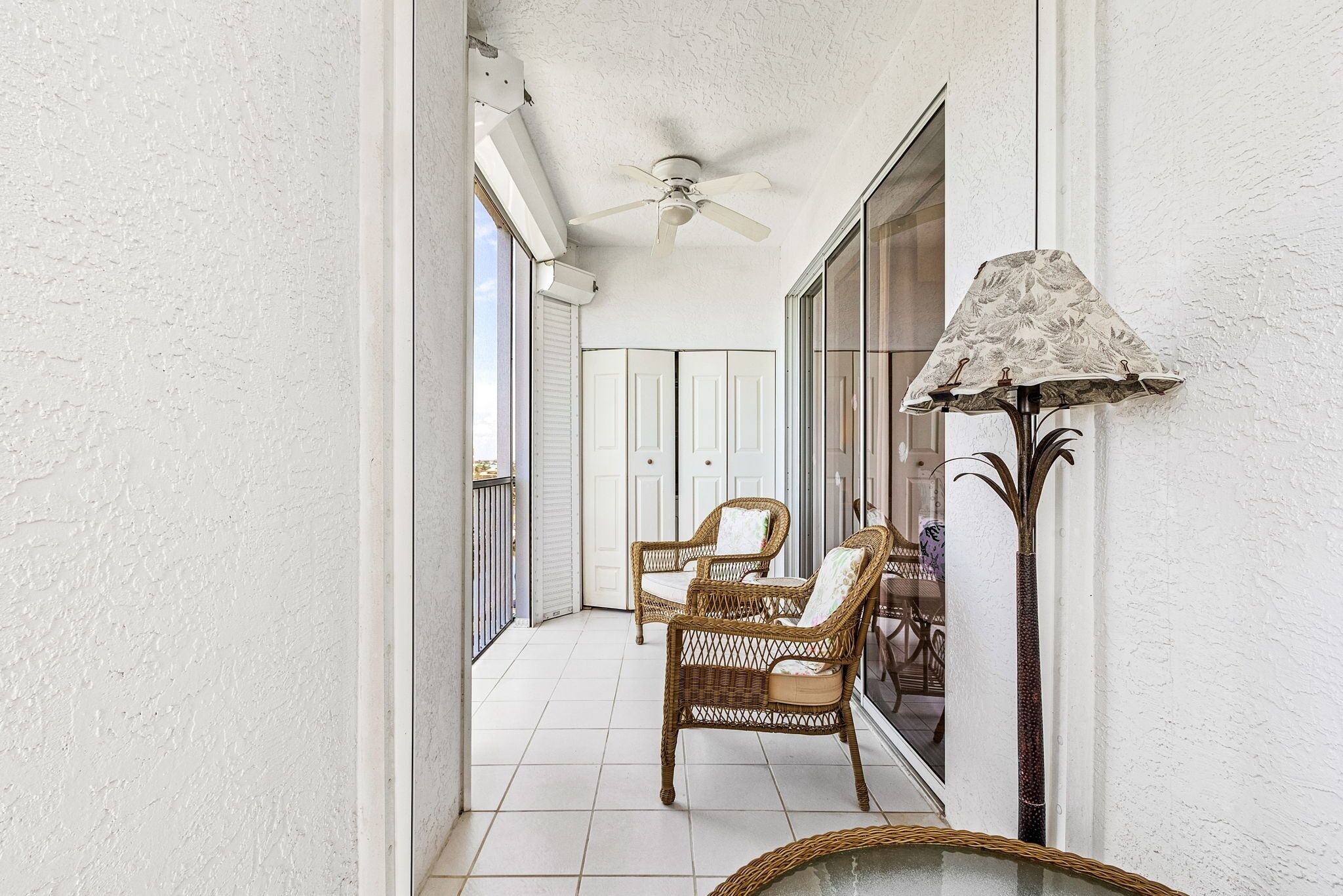 A balcony with wicker chairs, a ceiling fan, and a lamp.