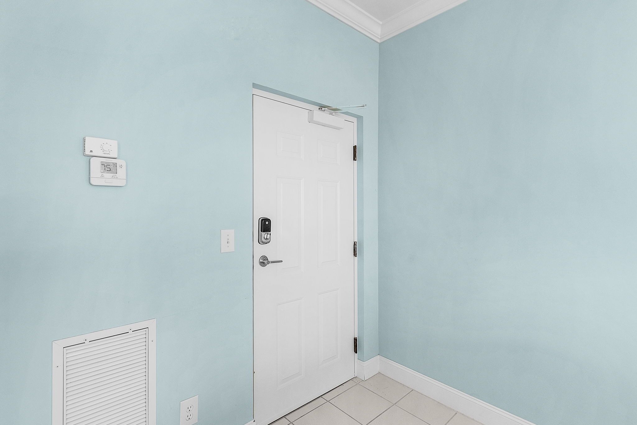 A hallway with a white door, a thermostat, and a vent on the wall.