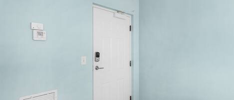 A hallway with a white door, a thermostat, and a vent on the wall.