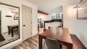 A spacious dining area with a wooden table and chairs, a kitchen with white cabinets, and a large mirror on the wall. - Snowlion Condos 103 2 Bedroom Condo (Vail)