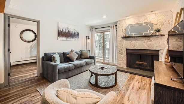 A modern living room with a fireplace, a sofa, a coffee table, and a view of the outdoors. - Snowlion Condos 103 2 Bedroom Condo (Vail)