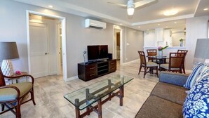 Una sala de estar con una mesa de centro de vidrio, un sofá, un televisor y un comedor con sillas.