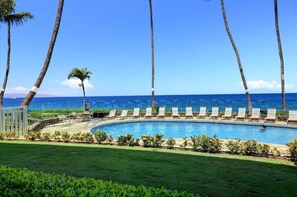 A pool area with lounge chairs and palm trees, overlooking a clear blue ocean.