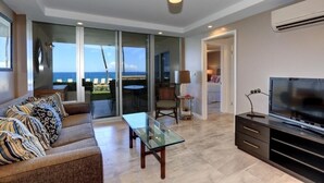 Una sala de estar moderna con sofá, una mesa de centro de vidrio, televisor y vista al mar.
