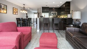 A modern kitchen with dark cabinets, a central island, and a dining area with red chairs. - Simba Run 1525 2 Bedroom Condo (Vail)