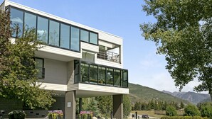 A modern two-story building with large windows and a balcony, surrounded by greenery and mountains in the background. - Simba Run 1525 2 Bedroom Condo (Vail)