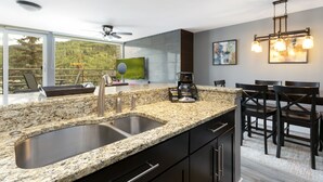 A modern kitchen with granite countertops, stainless steel sinks, and a dining area with dark wooden chairs and a table. - Simba Run 1525 2 Bedroom Condo (Vail)