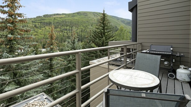 A balcony with a grill, a table, and chairs, overlooking a forested mountain. - Simba Run 1525 2 Bedroom Condo (Vail)