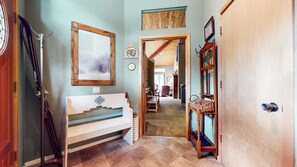 A room with a wooden bench, skis leaning against the wall, a framed picture, and a wooden door.