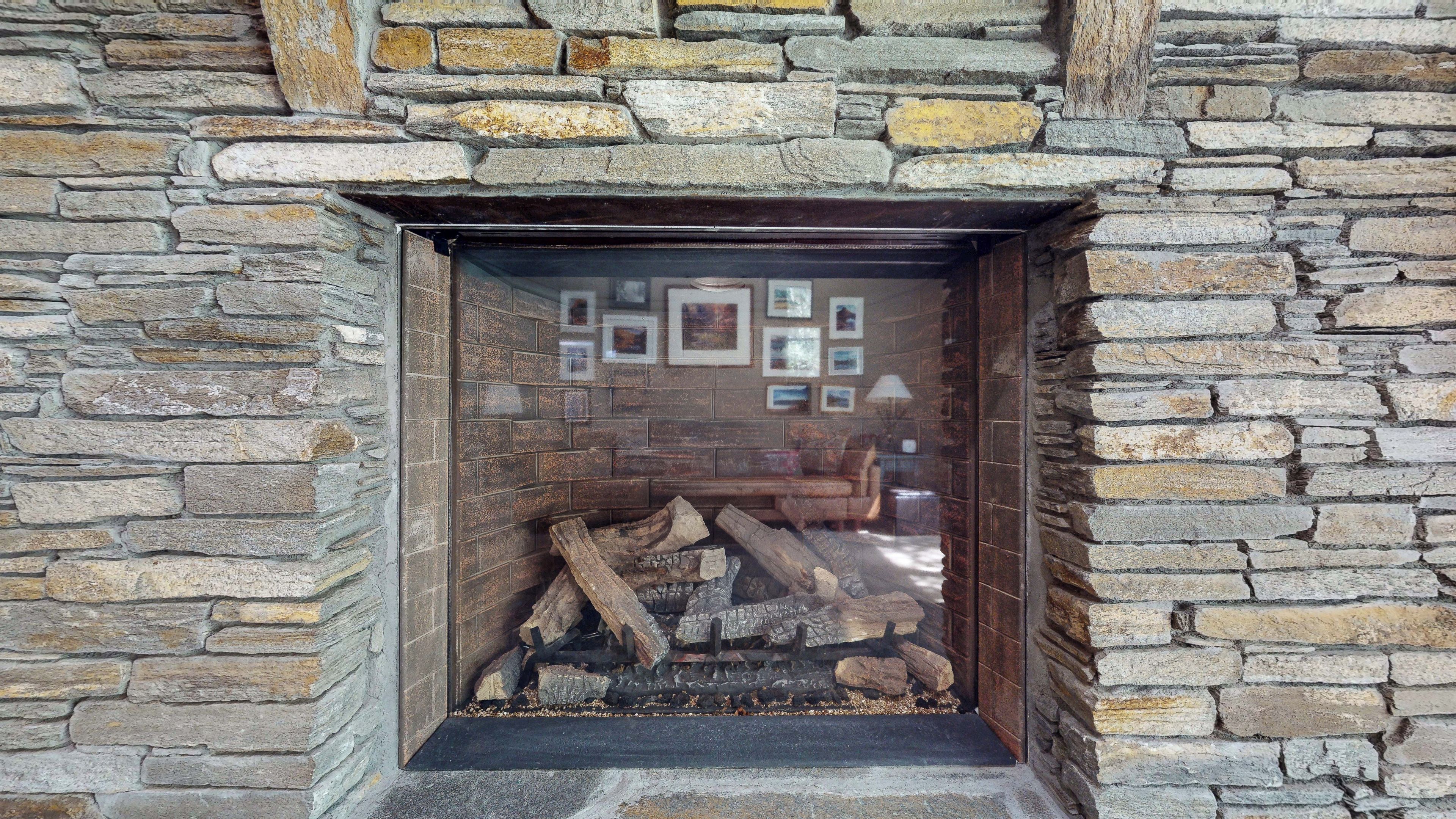 Pared de piedra con chimenea, enmarcada por un ventanal de vidrio.