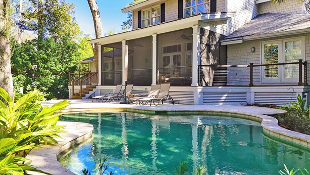 A house with a swimming pool, a covered patio with lounge chairs, and a view of the surrounding trees. - 58 Heritage Road - Harbour Town Golf Course Views & a Short Walk to the Beach (Hilton Head Island)