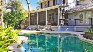 A house with a swimming pool, a covered patio with lounge chairs, and a view of the surrounding trees.