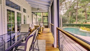 A covered porch with outdoor seating, a pool, and a view of the surrounding trees. - 58 Heritage Road - Harbour Town Golf Course Views & a Short Walk to the Beach (Hilton Head Island)