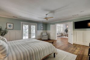 Un dormitorio con cama, una silla, ventilador de techo y televisor.