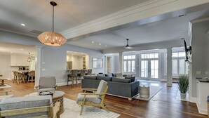A spacious living area with a large gray sectional sofa, wooden flooring, and a dining area with a round table and chairs. - 58 Heritage Road - Harbour Town Golf Course Views & a Short Walk to the Beach (Hilton Head Island)