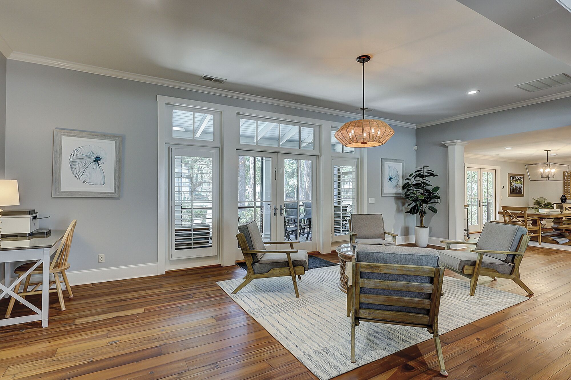 A spacious living room with hardwood floors, large windows, and a dining area with wooden furniture.