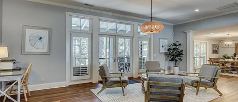 A spacious living room with hardwood floors, large windows, and a dining area with wooden furniture.