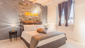 A modern bedroom with a stone accent wall, a neon sign, a bed with multiple pillows, bedside lamps, and a window with curtains. - Residence Piccolo Lord 2 - Italian Homing (Calcinato)